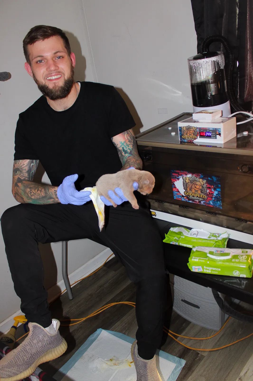 Logan Folse holding a newborn lilac English Bulldog puppy beside the Godspeed incubator
